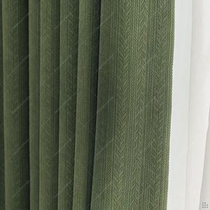 Puede incluir: Un juego de cortinas de color verde oliva con un patrón de textura de espiga vertical. La tela está plisada para crear pliegues profundos y uniformes que van de arriba a abajo, con un panel de tela blanca lisa visible en el borde derecho.