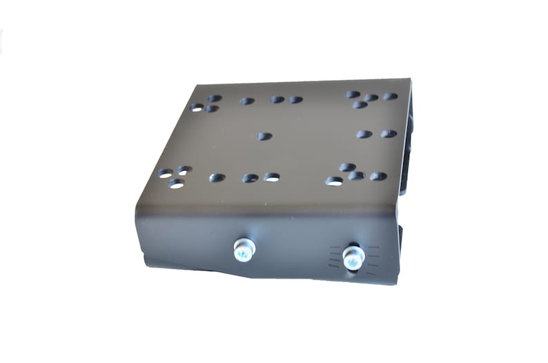 May include: A matte black metal mounting bracket featuring a flat rectangular top surface with multiple circular pre-drilled holes arranged in clusters. The front vertical edge includes two silver-colored cylindrical bolts with hex heads.