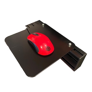 May include: A black metal computer mouse platform with a red mouse. The platform has a rectangular shape with a built-in tray and is secured with screws. The red mouse has a black logo.