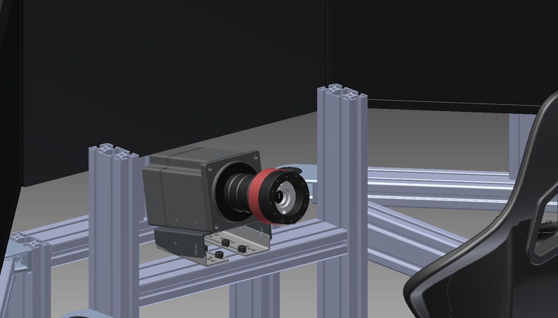 May include: A gray industrial camera with a black lens and a red ring mount, secured to a silver aluminum extrusion frame. The camera is positioned horizontally, featuring a metallic mounting bracket attached to the structural metal beams.