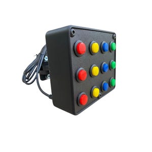 May include: A black control box with a grid of colorful buttons. The buttons are red, yellow, blue, and green. A power cord and plug extend from the side of the box. The buttons are arranged in three rows of four.