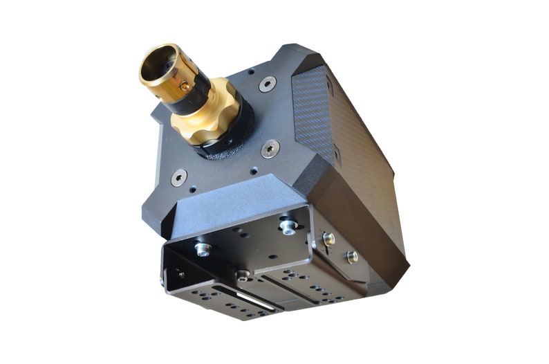 May include: A black racing wheel base featuring a gold-colored quick-release mechanism at the front. The unit has a textured carbon fiber-style side panel, multiple exposed silver hex bolts, and a black metal mounting bracket with slotted holes.