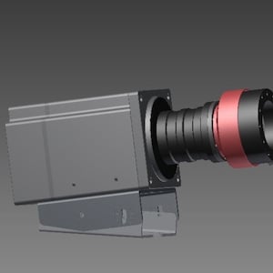 May include: A rectangular industrial camera housing in dark gray with a protruding black lens assembly featuring a prominent metallic copper-colored ring. The device is mounted on a matching gray metal bracket base with visible side screw holes.