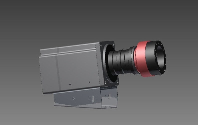 May include: A rectangular industrial camera housing in dark gray with a protruding black lens assembly featuring a prominent metallic copper-colored ring. The device is mounted on a matching gray metal bracket base with visible side screw holes.