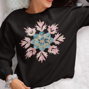 May include: Black sweatshirt with a pink and blue snowflake design. The snowflake is made of watercolor and glitter.