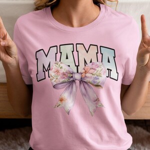 Peut inclure: T-shirt rose avec le mot "MAMA" en lettres arc-en-ciel et un grand n&oelig;ud floral.