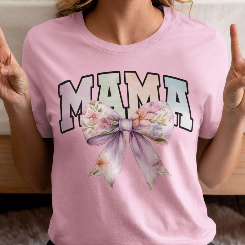 Peut inclure: T-shirt rose avec le mot "MAMA" en lettres arc-en-ciel et un grand n&oelig;ud floral.