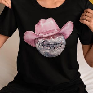 May include: A black t-shirt with a pink cowboy hat and a silver disco ball design.