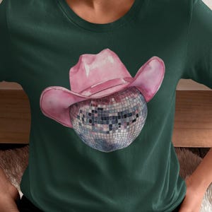 May include: A green t-shirt with a pink cowboy hat and a silver disco ball.