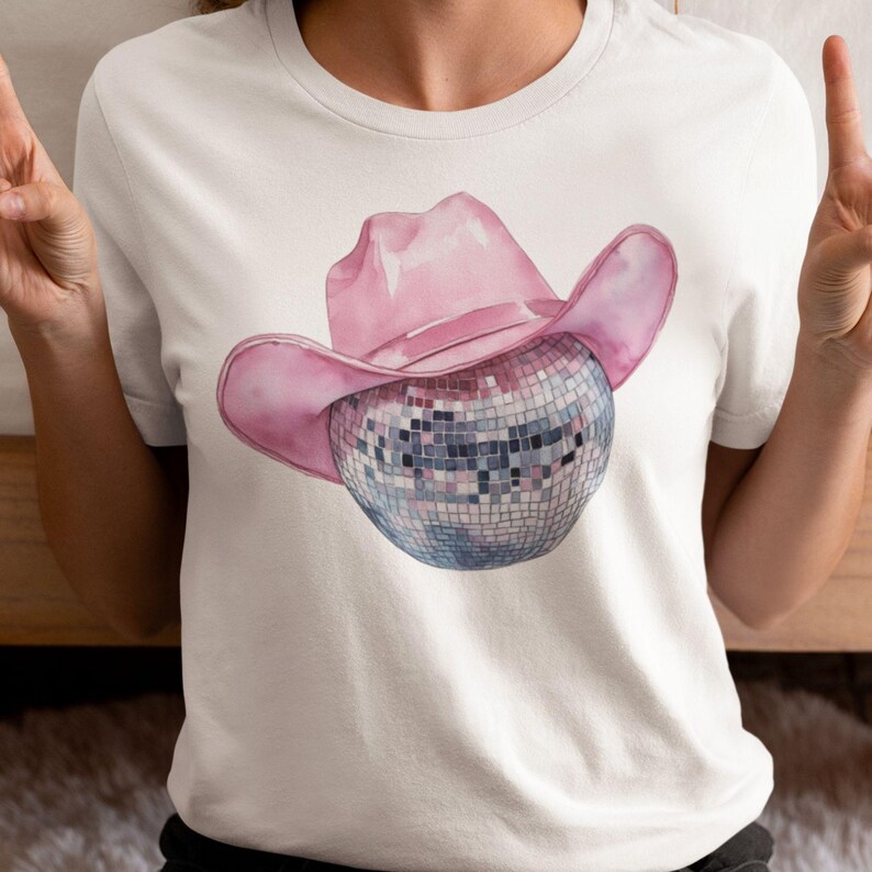 May include: A white t-shirt with a pink cowboy hat and a silver disco ball.
