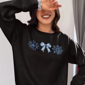 May include: Black sweatshirt with a blue snowflake and bow design.