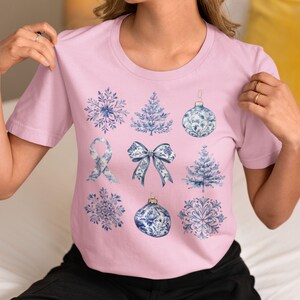 May include: A pink t-shirt with a blue and white snowflake, tree, bow, ornament, and ribbon design.