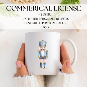 May include: White ceramic mug featuring a watercolor illustration of a toy nutcracker soldier in blue and gold. The mug has a curved handle and the text "COMMERICAL LICENSE" is at the top.