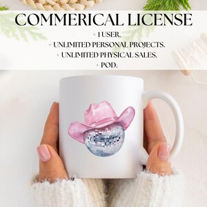 May include: A white ceramic mug with a pink cowboy hat on top of a silver disco ball. The mug is being held by a person wearing a white sweater.