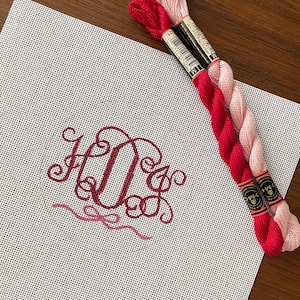 May include: A white Aida cloth with a red embroidered monogram "HOX" and two spools of embroidery floss, one red and one pink.