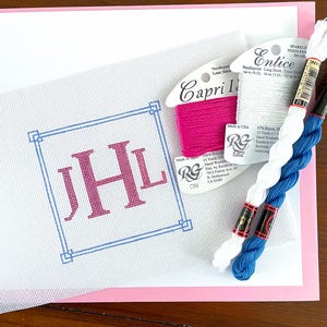 May include: Needlepoint kit featuring a white canvas with the initials "JHL" in pink within a blue square border. Includes pink, white, and blue embroidery floss, and a pink and white backing. The floss is labeled "Capri" and "Entice".