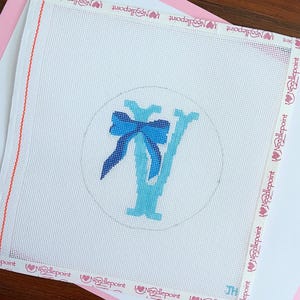 May include: Needlepoint canvas with a blue bow and the letter "Y" in shades of blue, within a circle. The canvas is white with a pink border and the words "Needlepoint" are printed on the edges.