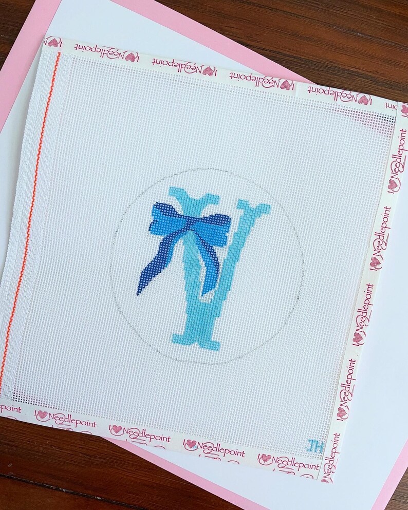 May include: Needlepoint canvas with a blue bow and the letter "Y" in shades of blue, within a circle. The canvas is white with a pink border and the words "Needlepoint" are printed on the edges.
