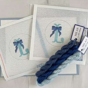 May include: Needlepoint kit featuring a monogrammed "L" with a bow in shades of blue. The kit includes canvas, thread, and tags. The canvas is white with a blue design. The thread is in various shades of blue.