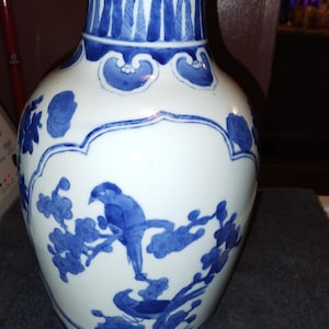 Puede incluir: Un jarrón de porcelana blanca con un diseño floral azul y blanco. El jarrón tiene una boca ancha y un cuello estrecho. El diseño presenta pájaros y flores.