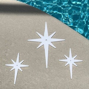May include: Three white starburst shapes with a hole in the center. The stars are different sizes and are arranged on a light gray surface.