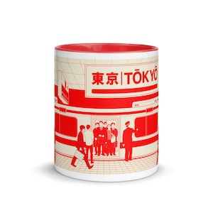 Op de afbeelding: Een witte keramische mok met een rode rand en een rode en witte illustratie van een treinstation in Tokio, Japan. De illustratie toont een trein met mensen die in- en uitstappen, en een bord met de tekst "Tokyo" in het Japans en Engels.