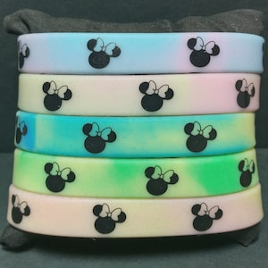 May include: A stack of six colorful silicone bracelets with a black and white Minnie Mouse design. The bracelets are in shades of blue, pink, green, and yellow.