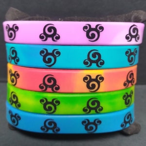 Op de afbeelding: Een stapel van vijf kleurrijke siliconen armbanden met een zwart swirl-ontwerp. De armbanden zijn in tinten roze, blauw, oranje, groen en lichtblauw.