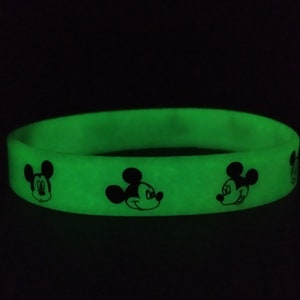 Puede incluir: Una pulsera de silicona verde brillante con dise&ntilde;os negros del personaje de Mickey Mouse. La pulsera es de color liso con la cara del personaje de dibujos animados impresa alrededor. La pulsera es un accesorio divertido.