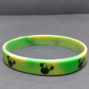 May include: A green and yellow silicone bracelet with a repeating pattern of black Mickey Mouse heads.