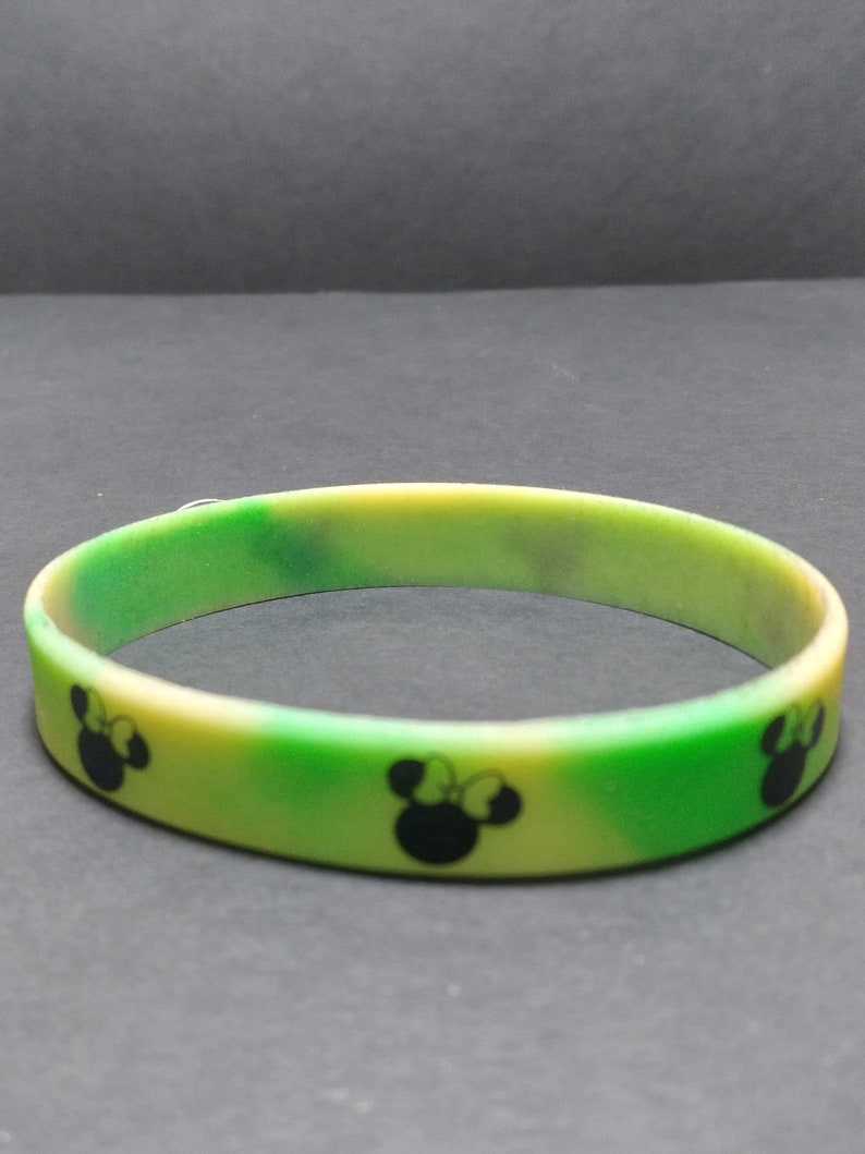 May include: A green and yellow silicone bracelet with a repeating pattern of black Mickey Mouse heads.