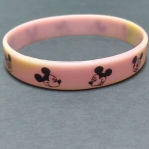 Puede incluir: Una pulsera de goma rosa y amarilla con dise&ntilde;os negros de Mickey Mouse. La pulsera es una banda s&oacute;lida con la cara del personaje de dibujos animados impresa alrededor de la circunferencia. El fondo es gris liso.