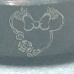 May include: A black ring with a white engraved design of a cartoon mouse with a bow and flowers.