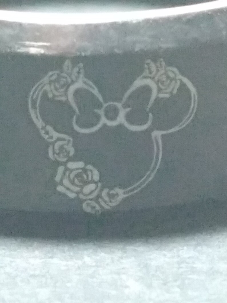 May include: A black ring with a white engraved design of a cartoon mouse with a bow and flowers.