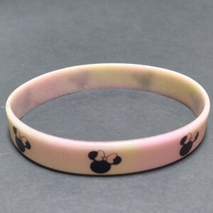 May include: A pink silicone bracelet with a faded ombre effect and black Mickey Mouse silhouettes.