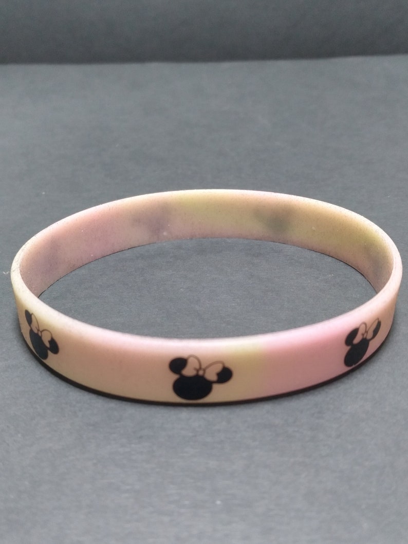May include: A pink silicone bracelet with a faded ombre effect and black Mickey Mouse silhouettes.