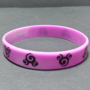 Op de afbeelding: Een paarse siliconen armband met zwarte swirl-ontwerpen.