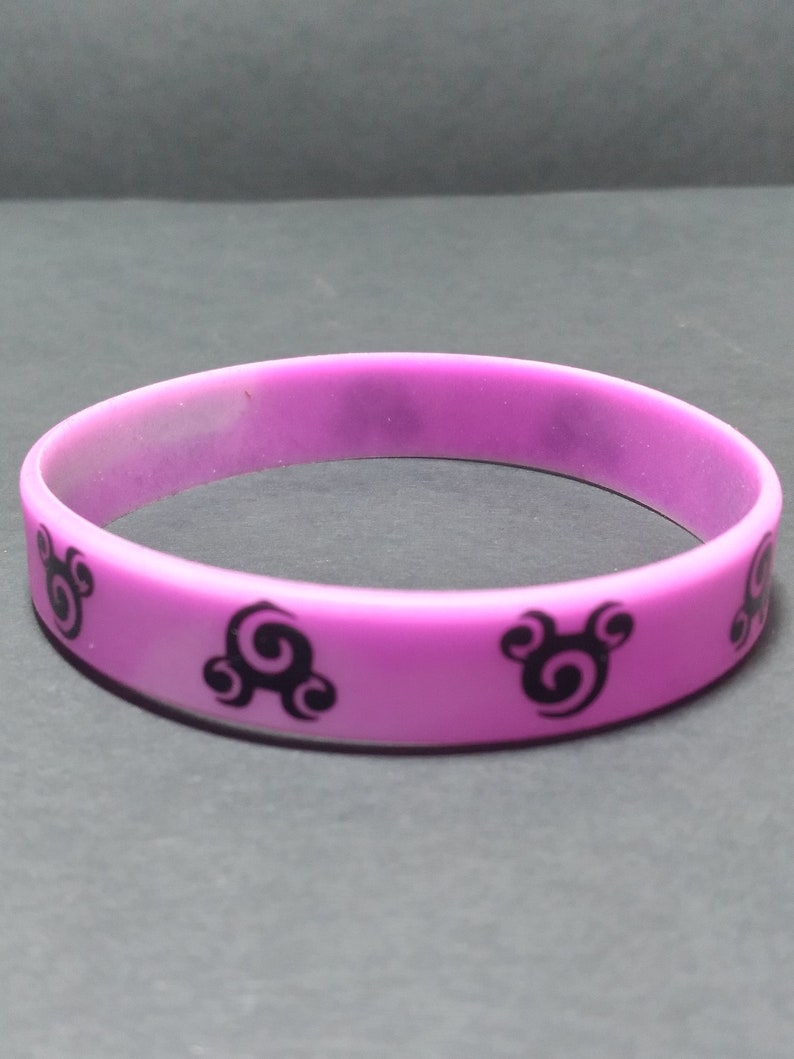 Op de afbeelding: Een paarse siliconen armband met zwarte swirl-ontwerpen.
