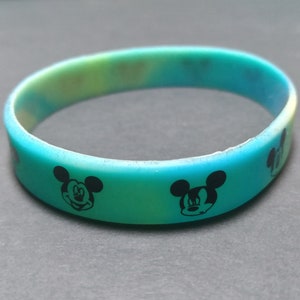 Puede incluir: Una pulsera de silicona multicolor con un degradado de azul, verde y amarillo. La pulsera presenta dise&ntilde;os negros del personaje de Mickey Mouse alrededor de la banda. Un accesorio divertido para los fan&aacute;ticos del ic&oacute;nico personaje de dibujos animados.