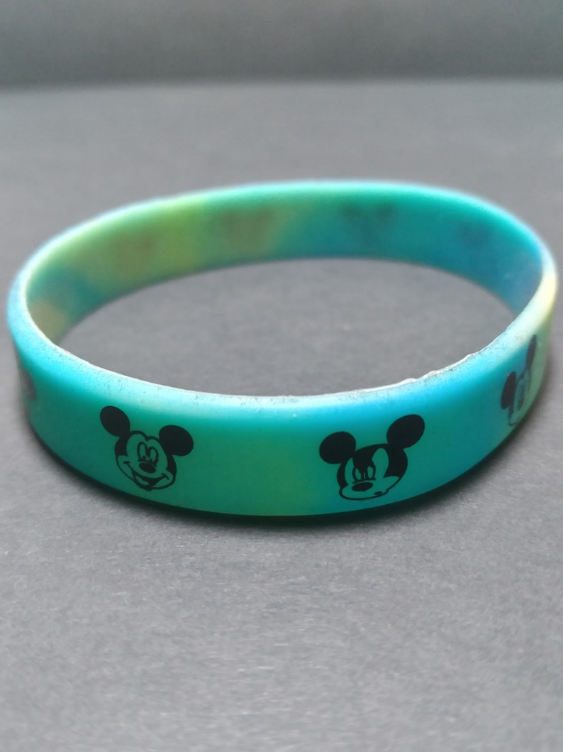 Puede incluir: Una pulsera de silicona multicolor con un degradado de azul, verde y amarillo. La pulsera presenta dise&ntilde;os negros del personaje de Mickey Mouse alrededor de la banda. Un accesorio divertido para los fan&aacute;ticos del ic&oacute;nico personaje de dibujos animados.
