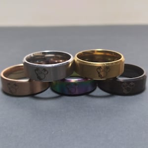 May include: Five stainless steel rings with a Mickey Mouse head design. The rings are in different colors: silver, gold, black, rose gold, and rainbow.