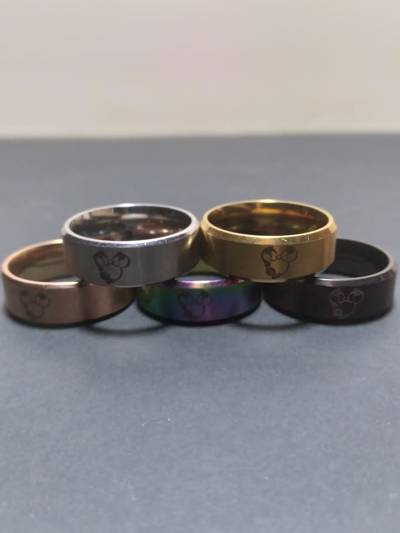 May include: Five stainless steel rings with a Mickey Mouse head design. The rings are in different colors: silver, gold, black, rose gold, and rainbow.