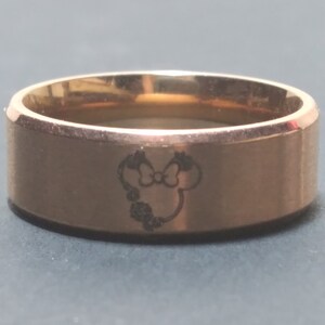 May include: A gold-toned stainless steel ring with a laser-engraved image of a cartoon mouse head with a bow.