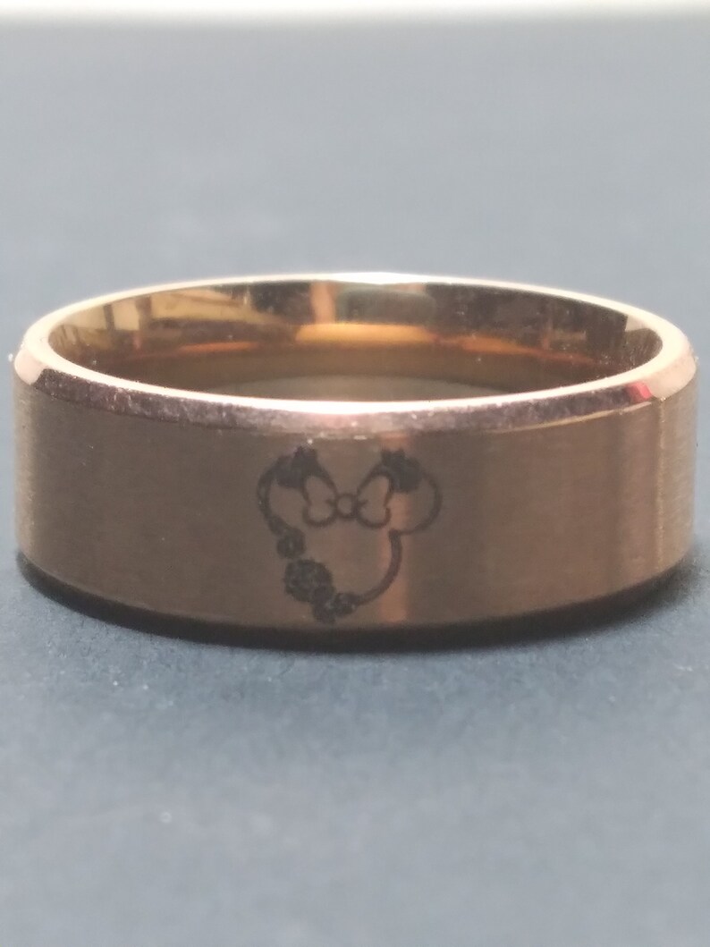 May include: A gold-toned stainless steel ring with a laser-engraved image of a cartoon mouse head with a bow.