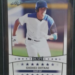 K&ouml;nnte beinhalten: Baseballkarte mit Shohei Ohtani in wei&szlig;-blauer Uniform, der auf einem Baseballfeld rennt. Die Karte zeigt das Wort "DRAFT" sowie den Namen und die Position des Spielers, RHP/OF. Die Karte befindet sich in einer Schutzh&uuml;lle.