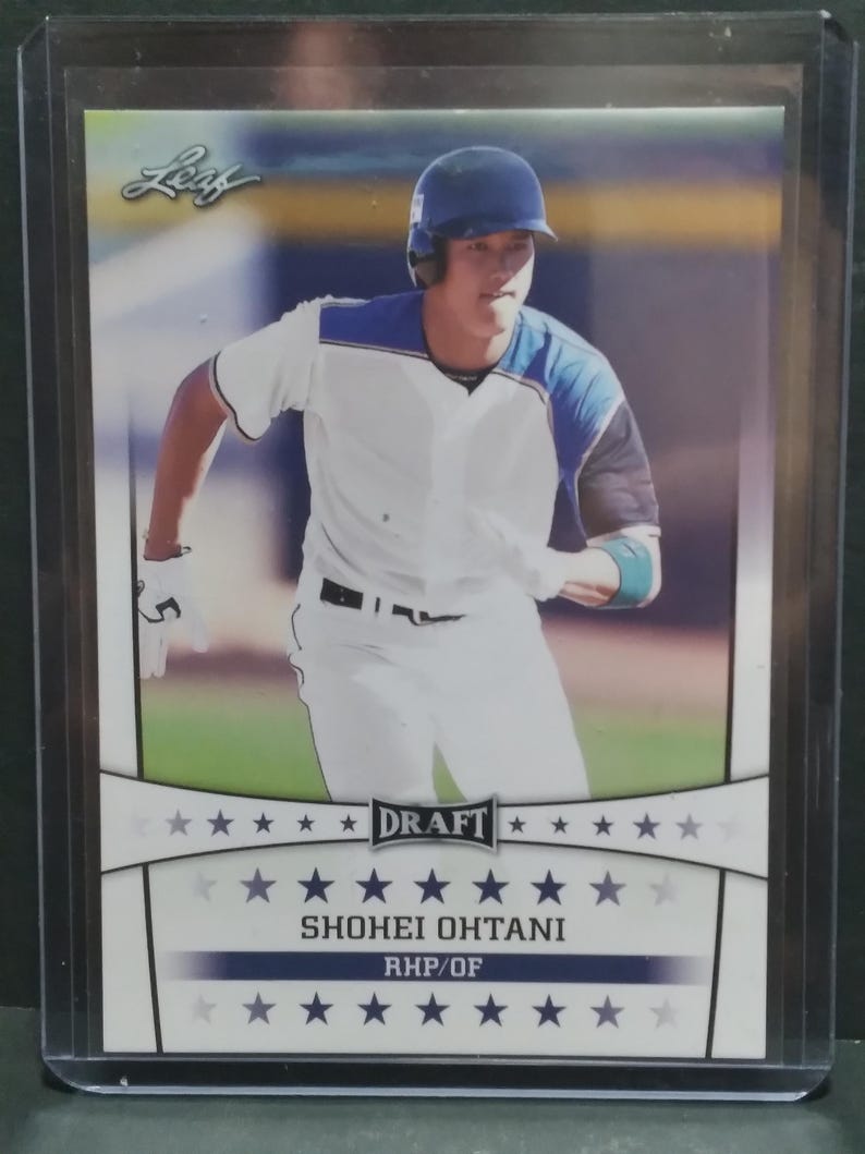K&ouml;nnte beinhalten: Baseballkarte mit Shohei Ohtani in wei&szlig;-blauer Uniform, der auf einem Baseballfeld rennt. Die Karte zeigt das Wort "DRAFT" sowie den Namen und die Position des Spielers, RHP/OF. Die Karte befindet sich in einer Schutzh&uuml;lle.