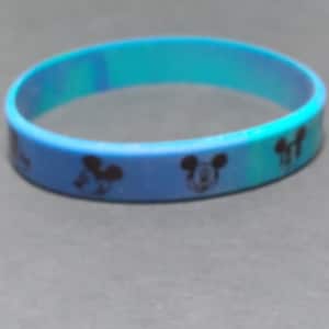 Puede incluir: Una pulsera de silicona azul con un patr&oacute;n repetido de cabezas de Mickey Mouse negras.