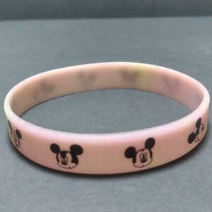Puede incluir: Una pulsera de silicona rosa claro con caras negras de Mickey Mouse. La pulsera es una banda s&oacute;lida, con la cara del personaje de dibujos animados repiti&eacute;ndose alrededor de la circunferencia. Un accesorio sencillo e informal.