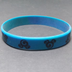 Op de afbeelding: Een blauwe siliconen armband met een zwart swirl-ontwerp.