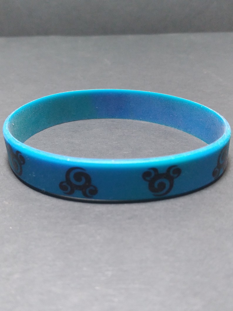 Op de afbeelding: Een blauwe siliconen armband met een zwart swirl-ontwerp.